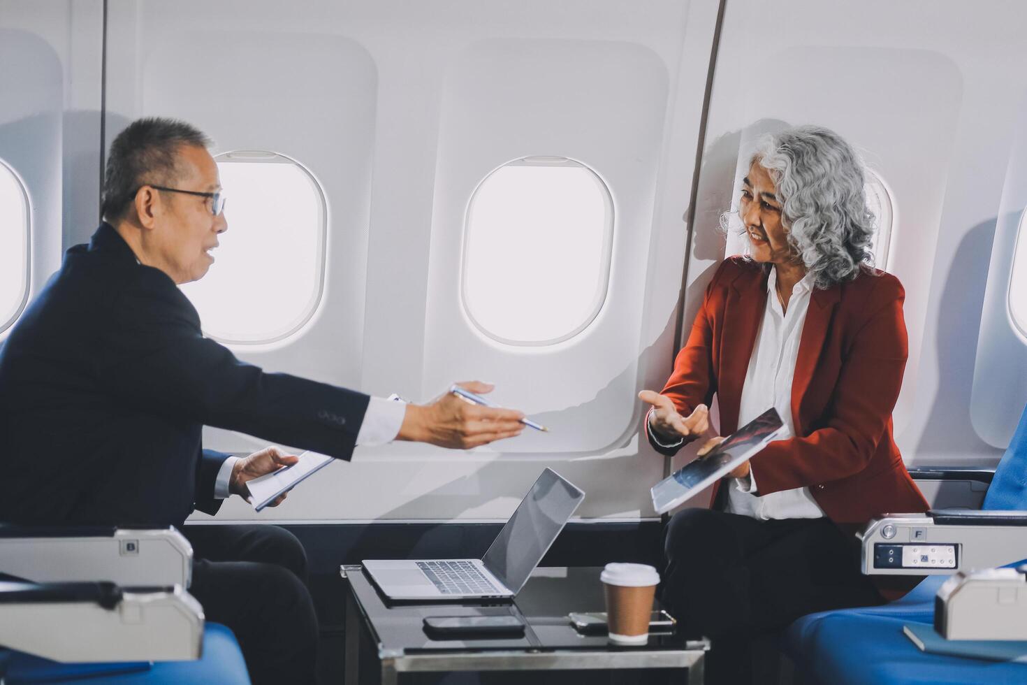 Two passengers looking at laptop together on board. Businessman in brown suit showing project on notebook to businessman with eyeglasses. Work and travel concept. photo