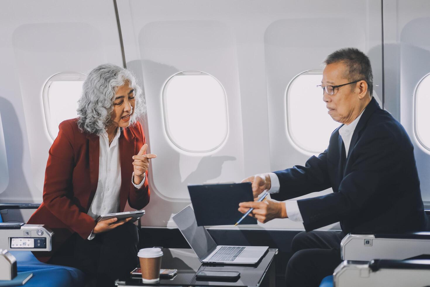 Two passengers looking at laptop together on board. Businessman in brown suit showing project on notebook to businessman with eyeglasses. Work and travel concept. photo