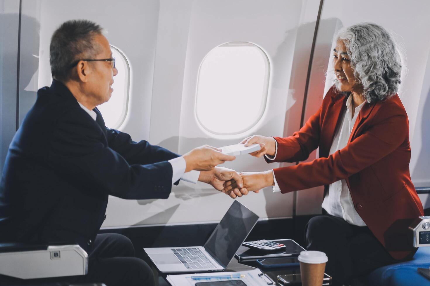 business people at meeting in private plane, Asian businessman in suit is talking to woman in jet and pointing at blank laptop screen, colleagues are discussing deal and flying in plane photo