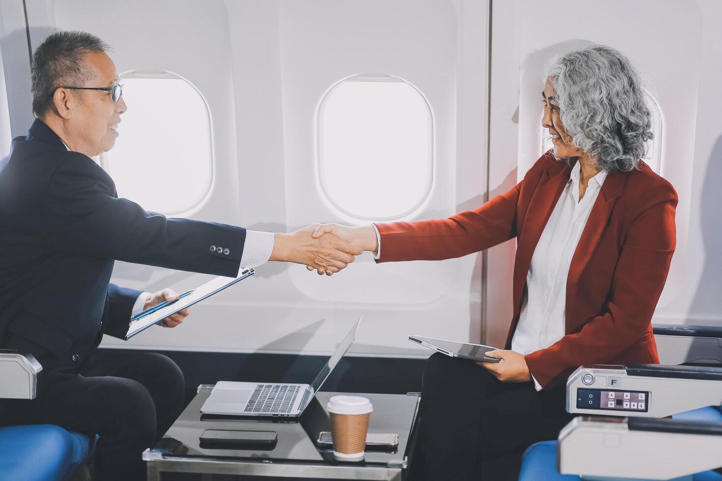 business people at meeting in private plane, Asian businessman in suit is talking to woman in jet and pointing at blank laptop screen, colleagues are discussing deal and flying in plane photo