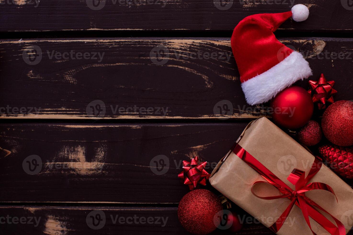 Top view photo Christmass flatlay gift box,Santa hat and red christmas tree toys on wooden background.. Xmas backdrop with space for text.Copyspace.