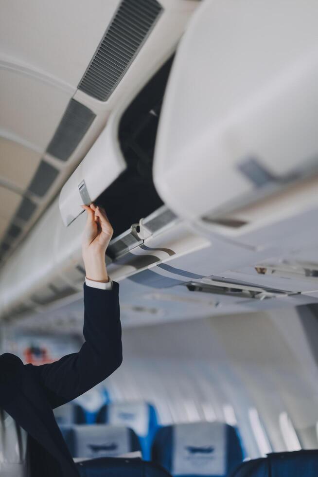 Asian female tourist packs her suitcase on a shelf inside the plane. photo