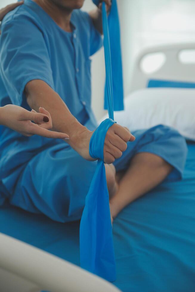 Close up hand patient doing stretching exercise with a flexible exercise band and a physical therapist hand to help in clinic room. photo