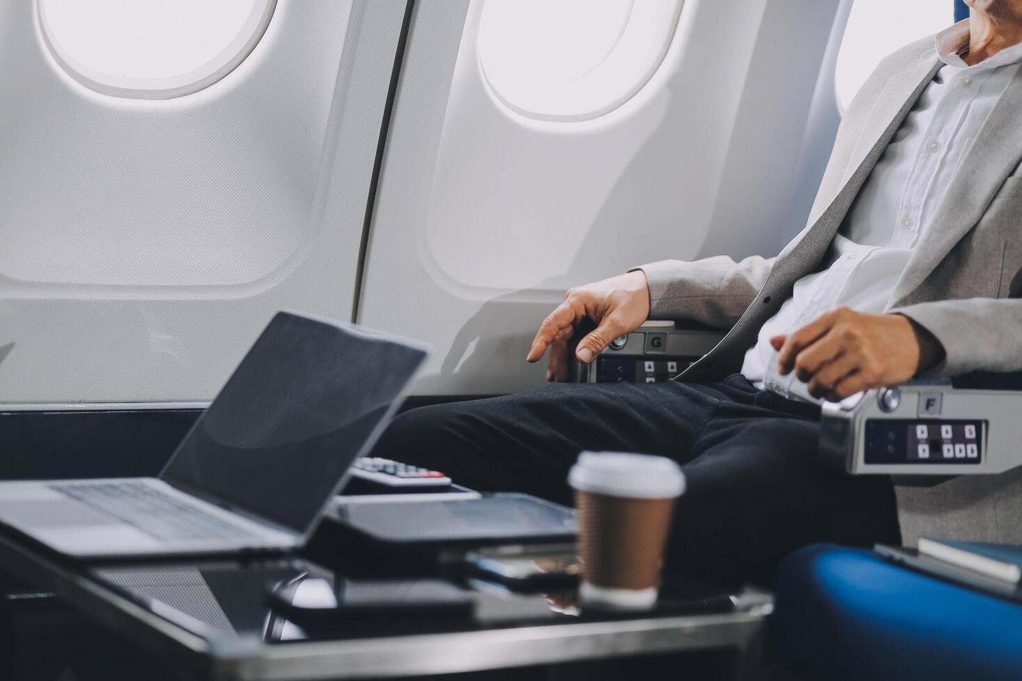 business people at meeting in private plane, Asian businessman in suit is talking to woman in jet and pointing at blank laptop screen, colleagues are discussing deal and flying in plane photo