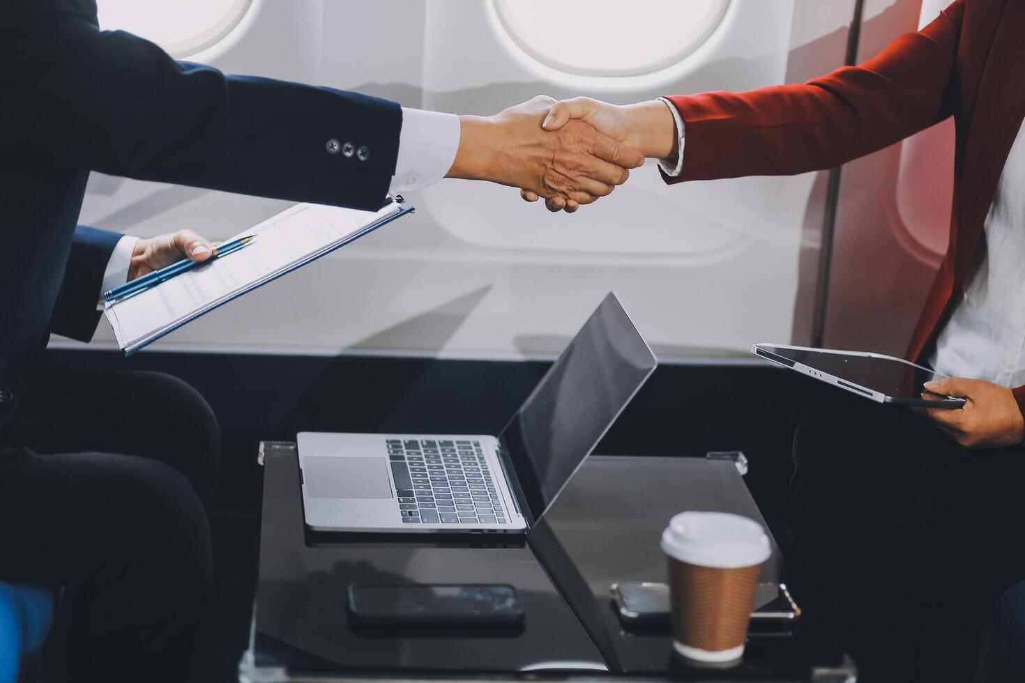business people at meeting in private plane, Asian businessman in suit is talking to woman in jet and pointing at blank laptop screen, colleagues are discussing deal and flying in plane photo