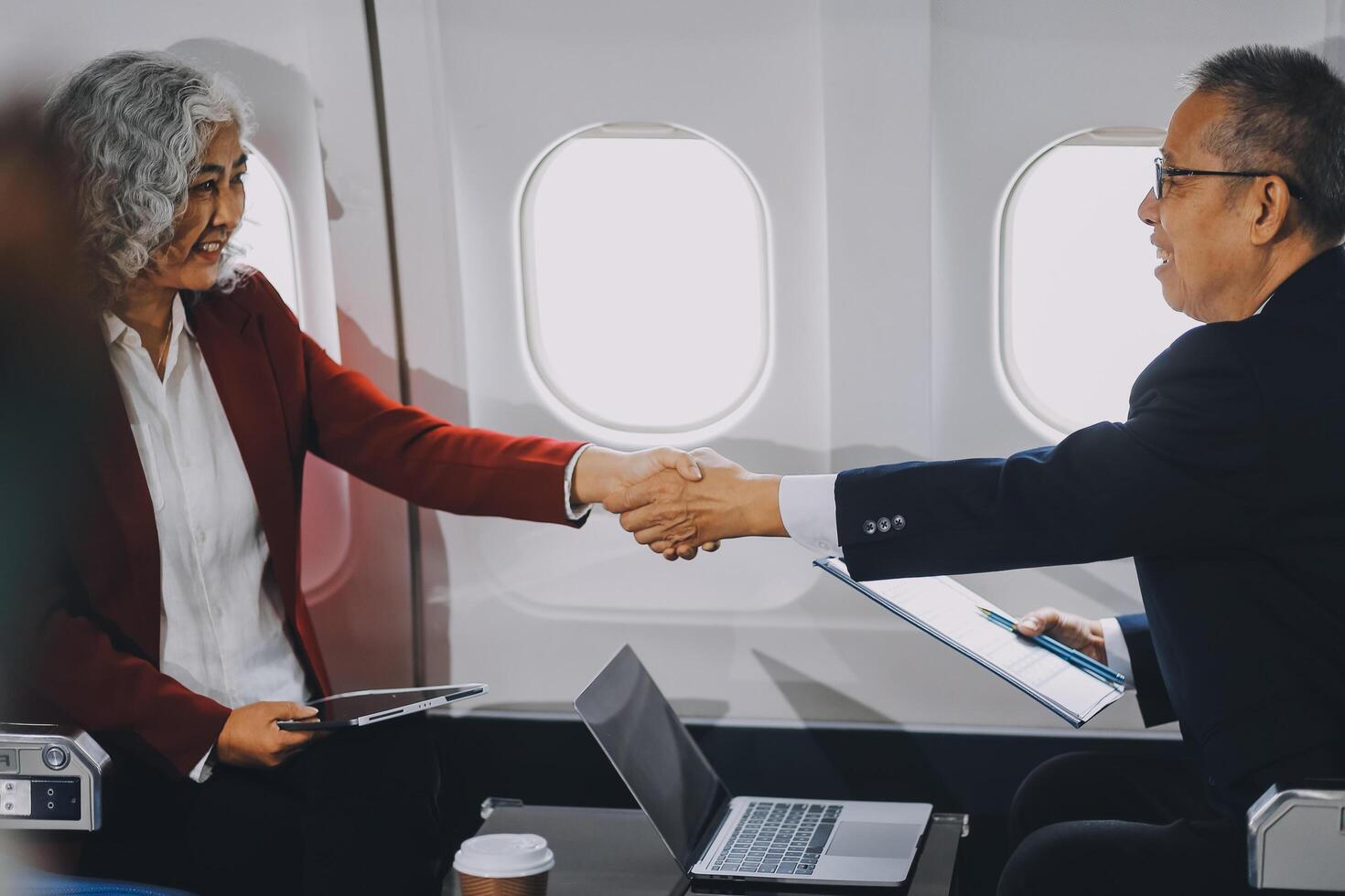 business people at meeting in private plane, Asian businessman in suit is talking to woman in jet and pointing at blank laptop screen, colleagues are discussing deal and flying in plane photo