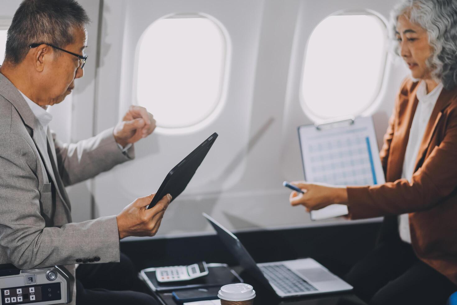 business people at meeting in private plane, Asian businessman in suit is talking to woman in jet and pointing at blank laptop screen, colleagues are discussing deal and flying in plane photo