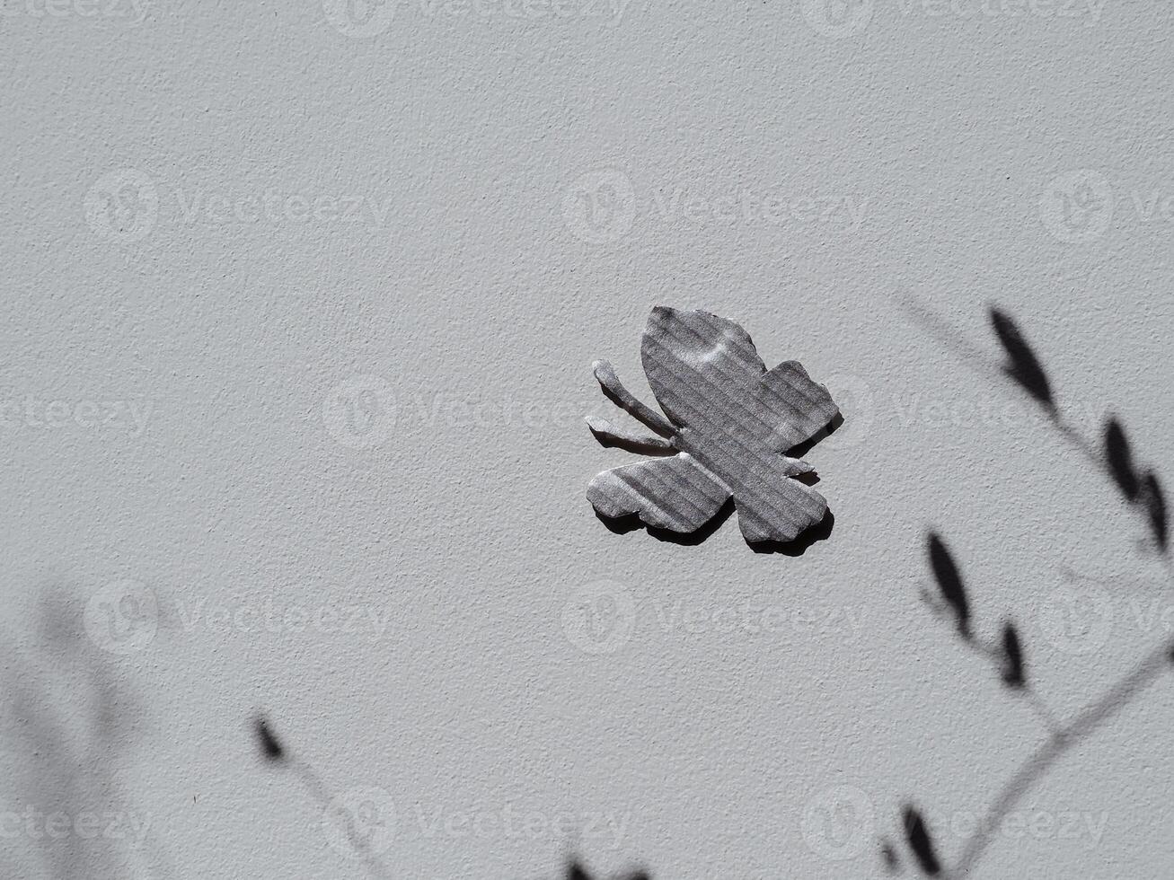 Silver painted cardboard butterfly on white wall and tree silhouette for copy space, nature and environment concept. photo
