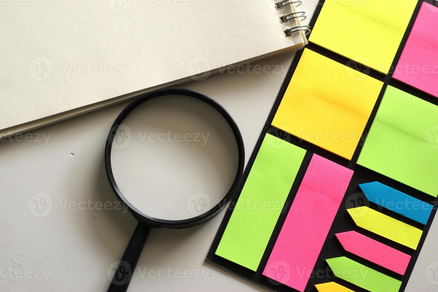 flat lay of notepad and magnifying glass and colorful sticky notes on white background photo