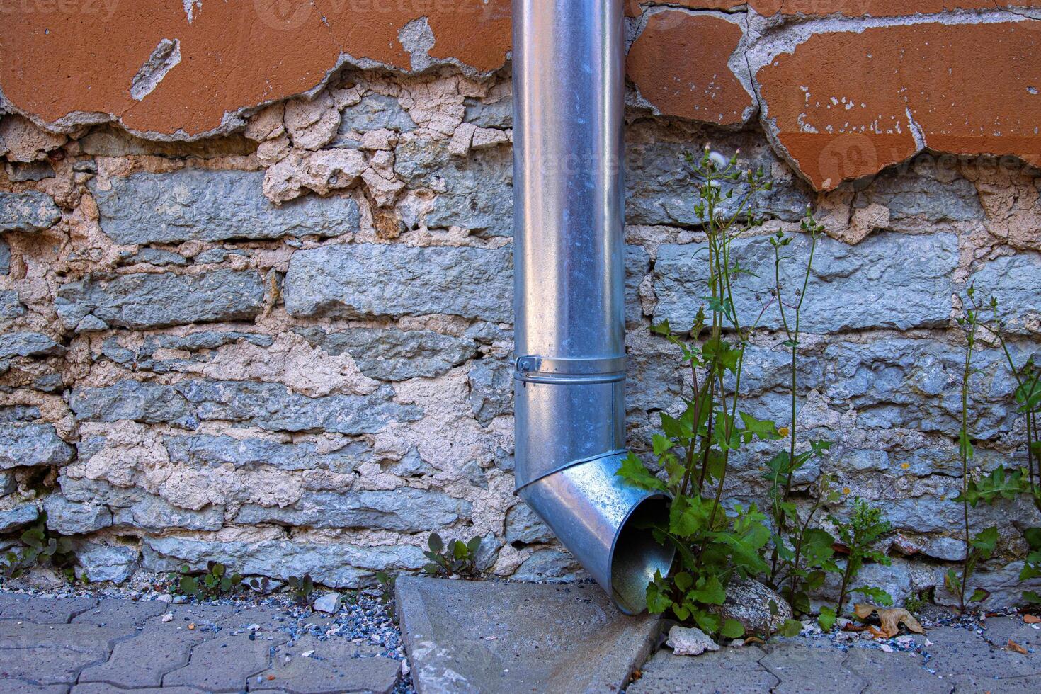 Galvanized metal downspout dreainpipe against an old weathered stone and cracked stucco wall. ideal for urban decay, architecture, and texture backgrounds. Copy space photo