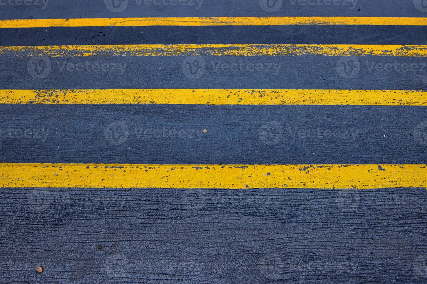 Closeup of a textured asphalt road with weathered yellow stripes on a rough gray pavement, great for use in street photography, urban design, or traffic-related visuals. Copy space photo