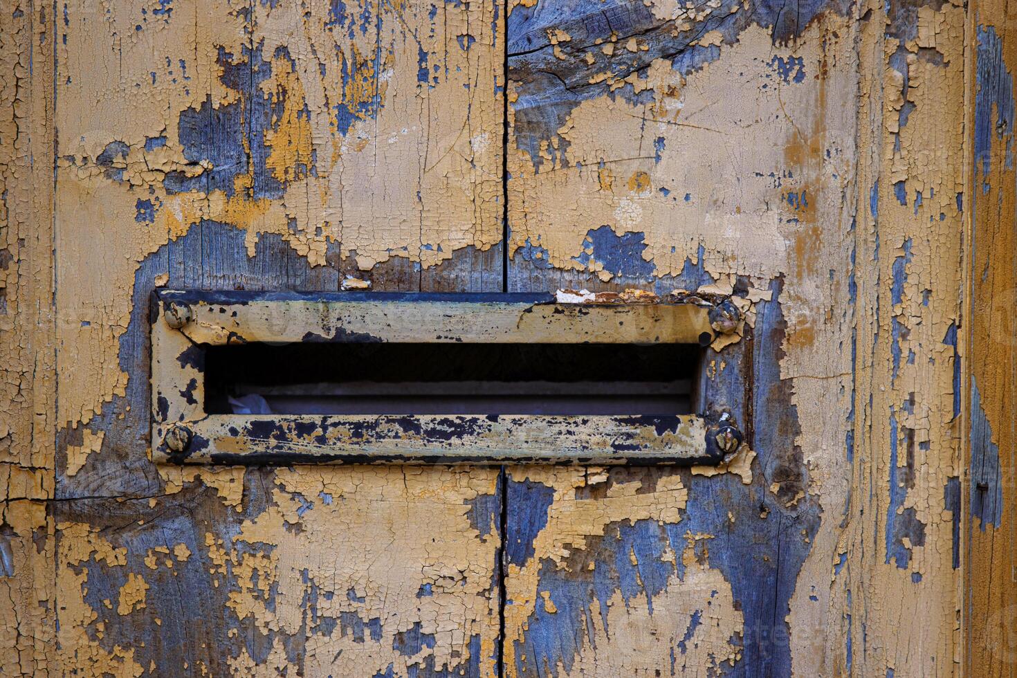 Closeup image of a weathered, peeling paint on an old wooden door with a vintage mail slot, perfect for backgrounds, textures, and rustic-themed designs. Copy space photo