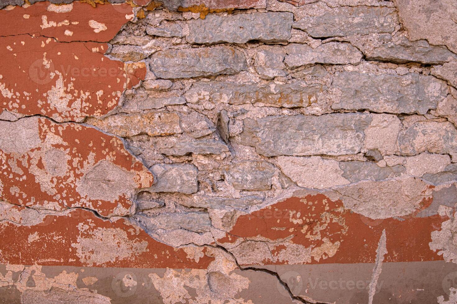 Cracked wall with rustic charm. A detailed close-up of a weathered wall with peeling red paint, revealing layers of plaster and brick underneath. Copy space photo