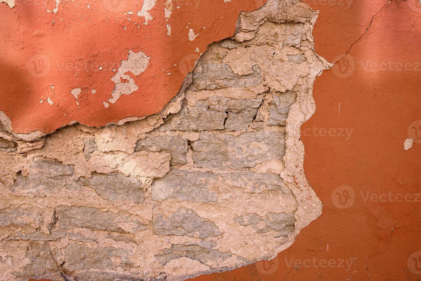 Cracked wall with rustic charm. A detailed close-up of a weathered wall with peeling red paint, revealing layers of plaster and brick underneath. Copy space photo