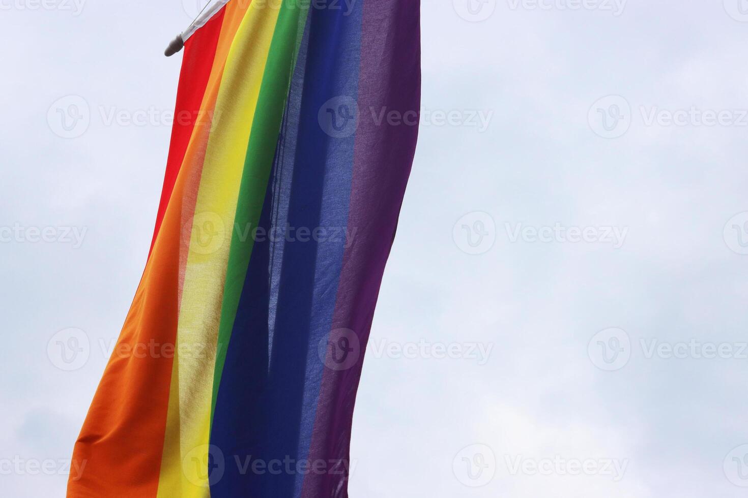 Fragment of the rainbow flag, a symbol for the LGBT community, hanging waving in the wind with a cloudy sky background photo