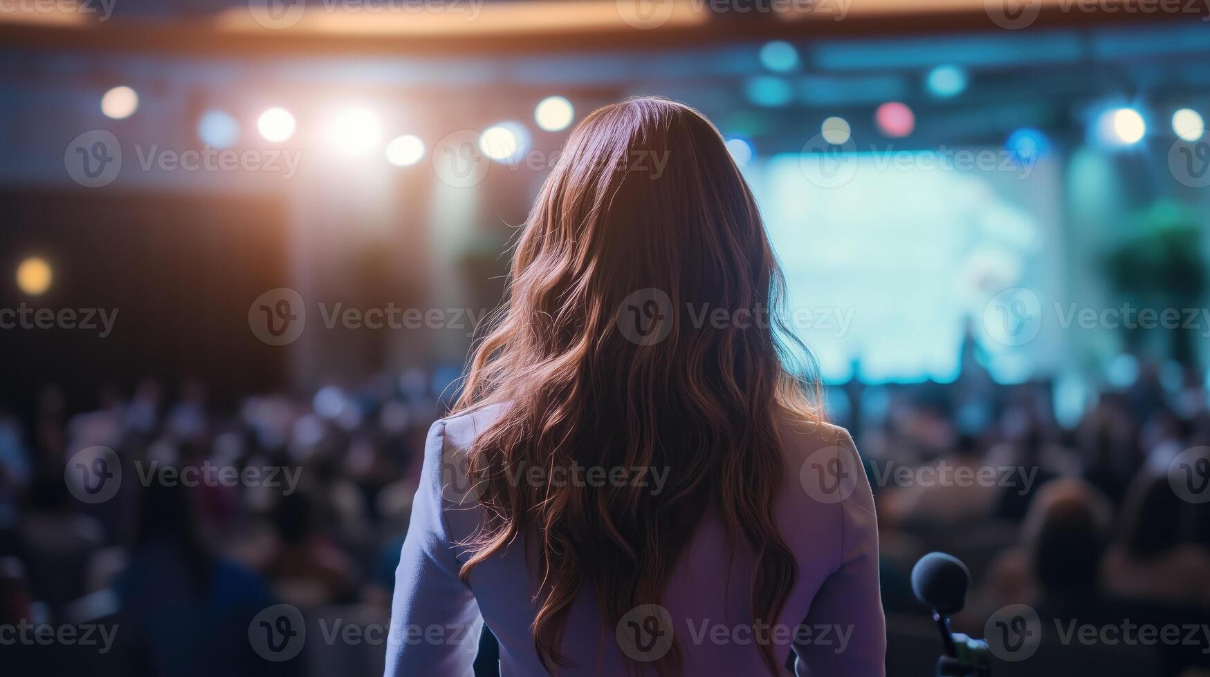 Female Speaker Addressing a Large Audience on Stage at a Conference or Event photo