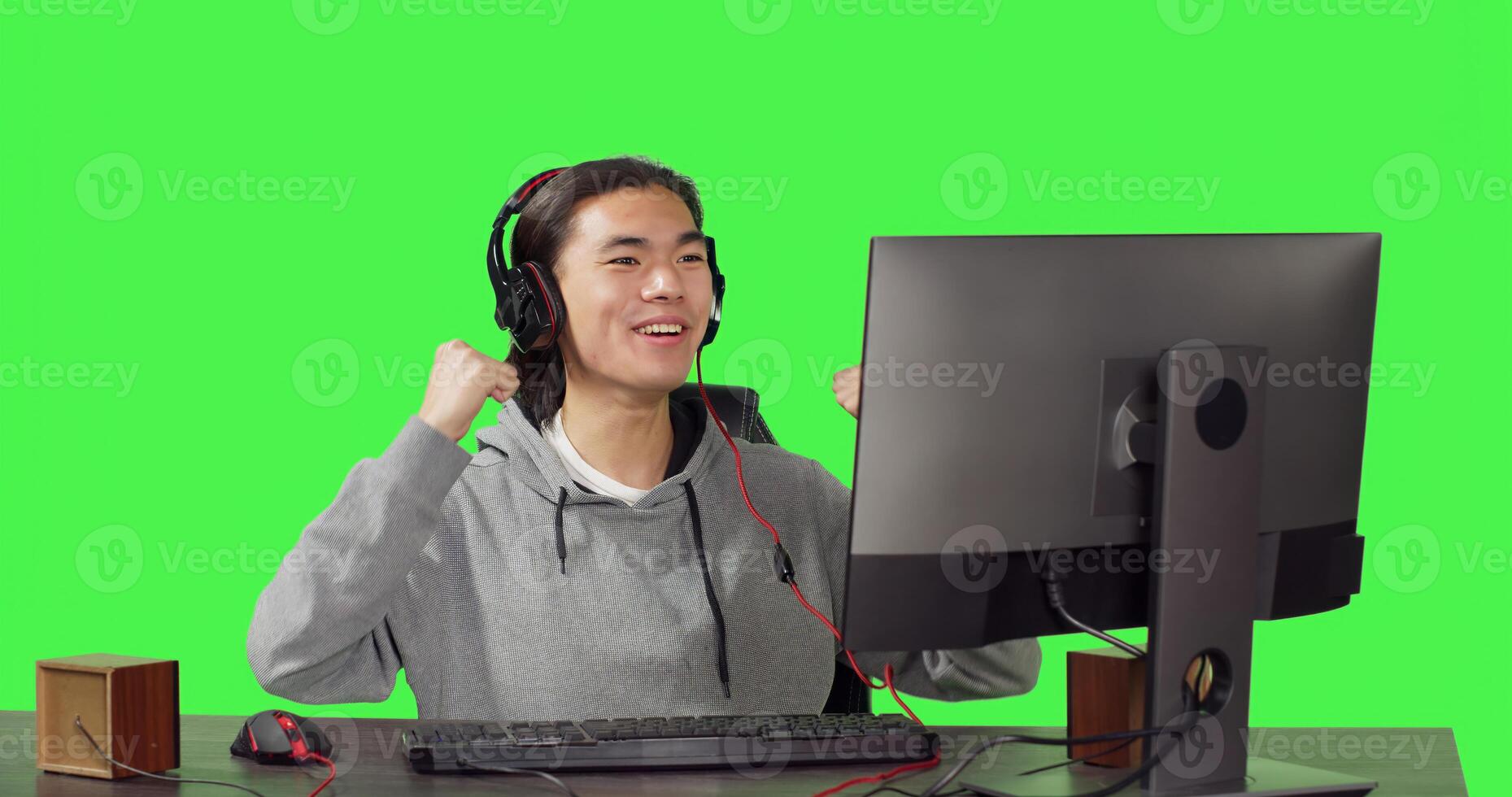 Asian person being on computer at desk, playing online rpg games with his friends. Young man having fun with new web contest, talking to people on headset over greenscreen backdrop. photo