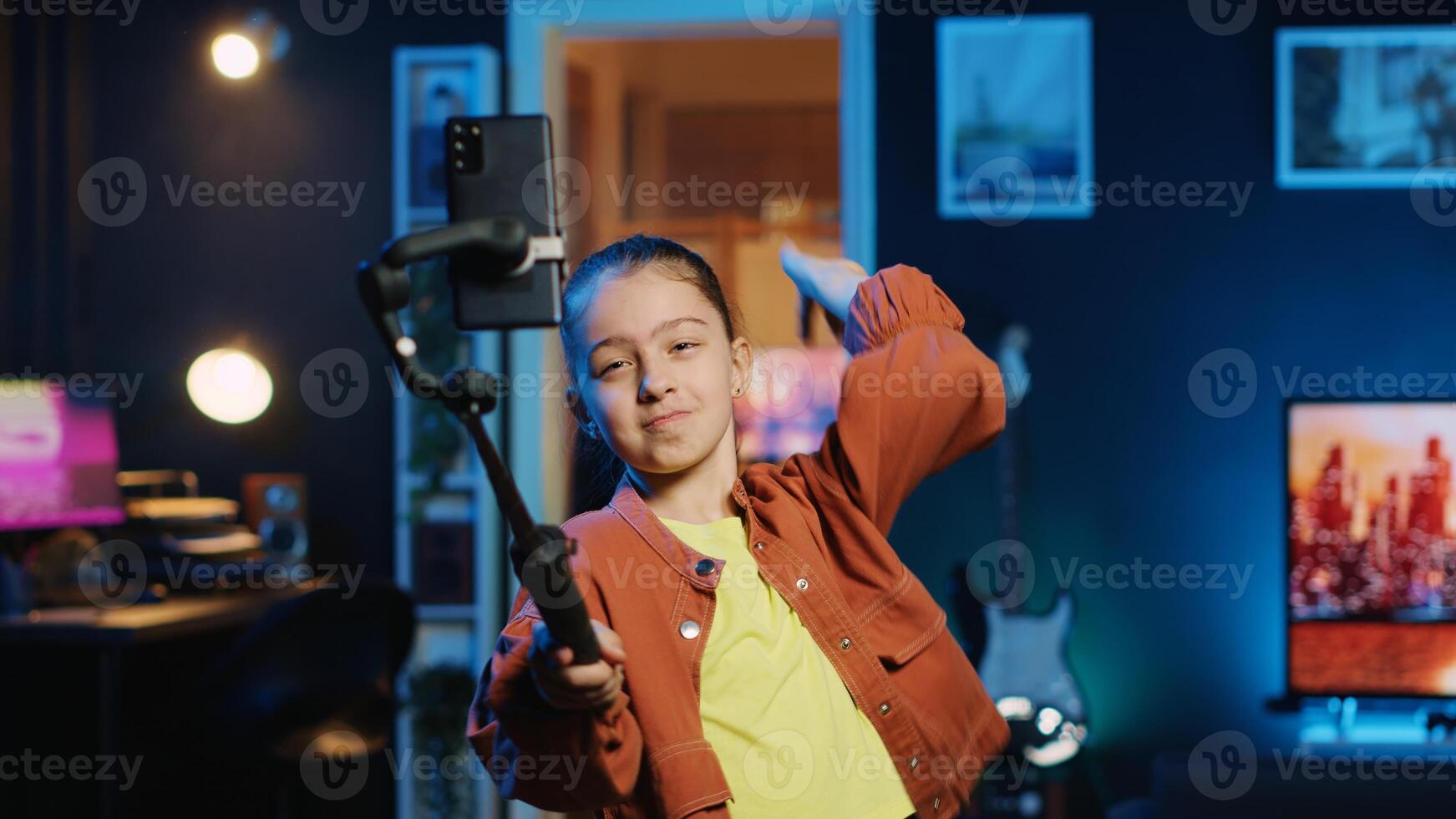 Happy child taking part in viral dance craze after seeing favorite celebrities doing it, filming with smartphone attached to selfie stick, doing trendy challenge for online fans photo