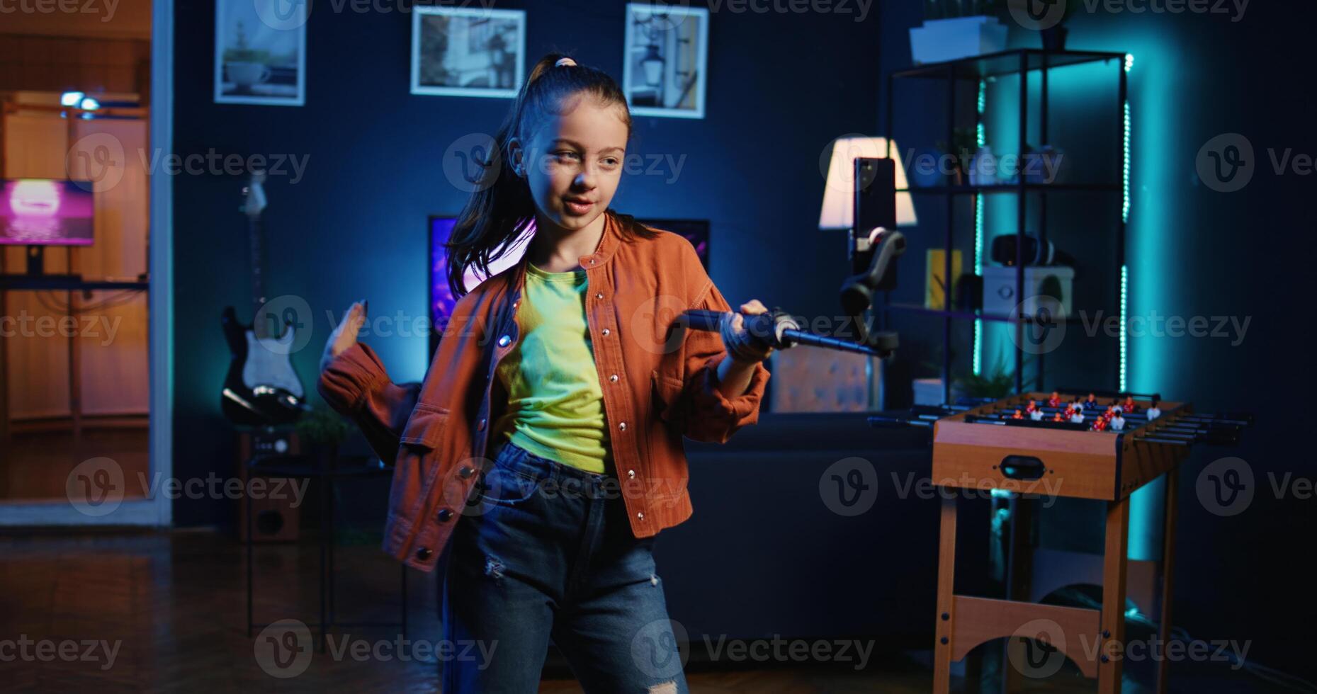 Talented kid using smartphone on selfie stick to film dance tutorial for other children watching her online social media content. Joyous little media star recording targeting generation Z fans photo
