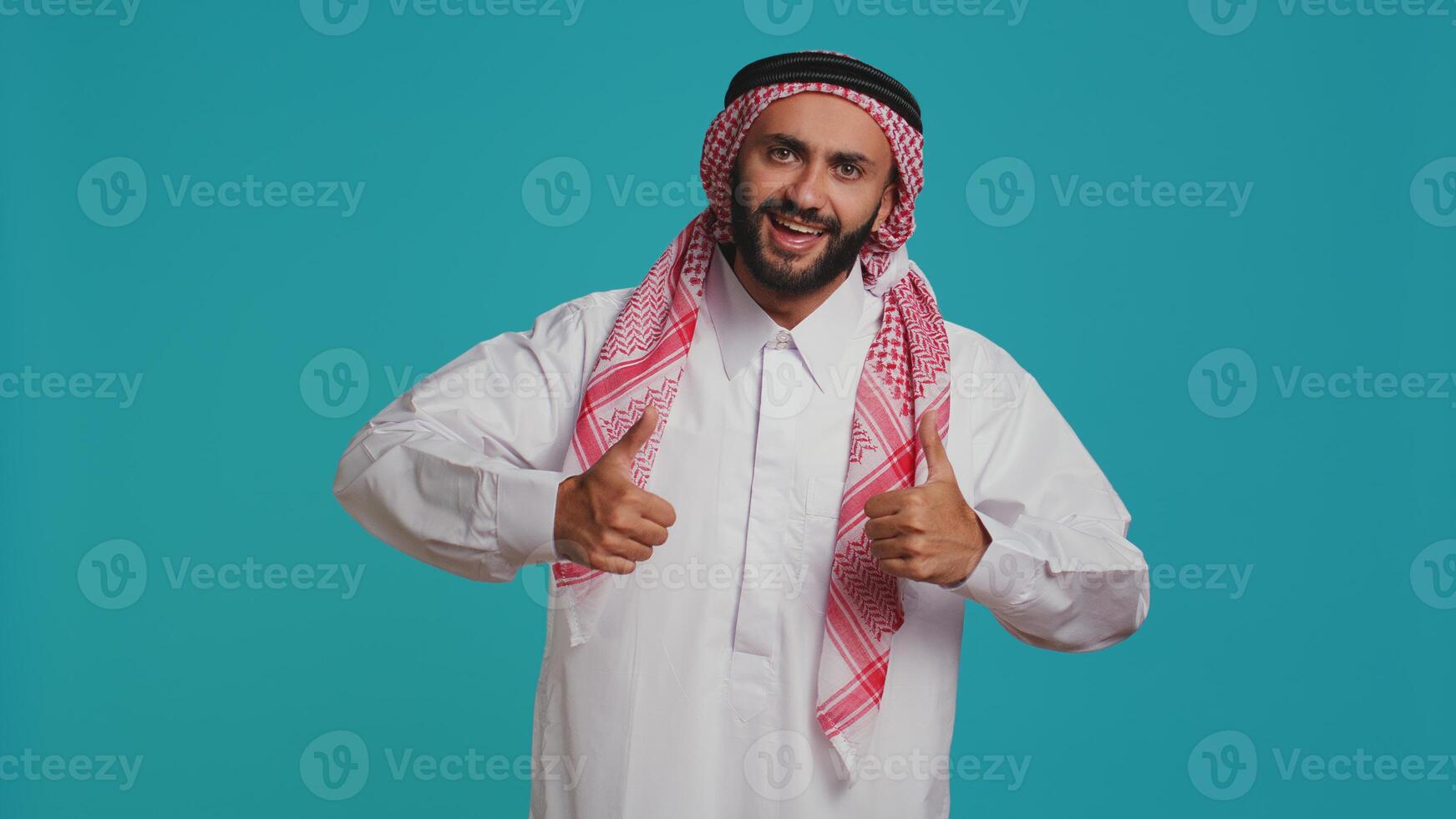 Person wearing customary thobe and kufiyah seems joyful, exhibiting genuine muslim beliefs and practices. Middle eastern guy with distinctive culture, dress and structured scarf. photo