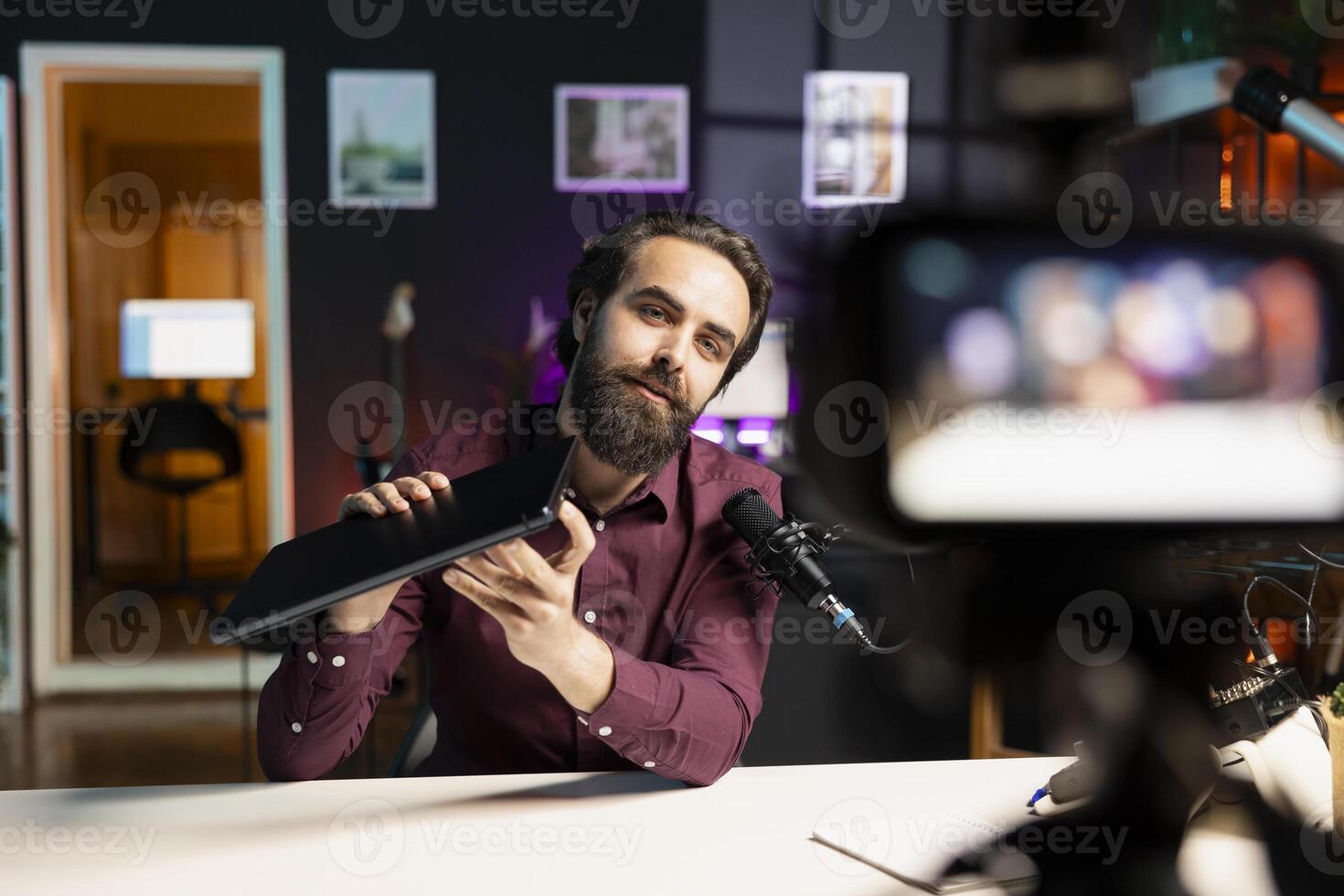 Man presenting laptop to audience, filming with professional camera and mic. Content creator assessing notebook product, recording with specialized equipment in studio photo