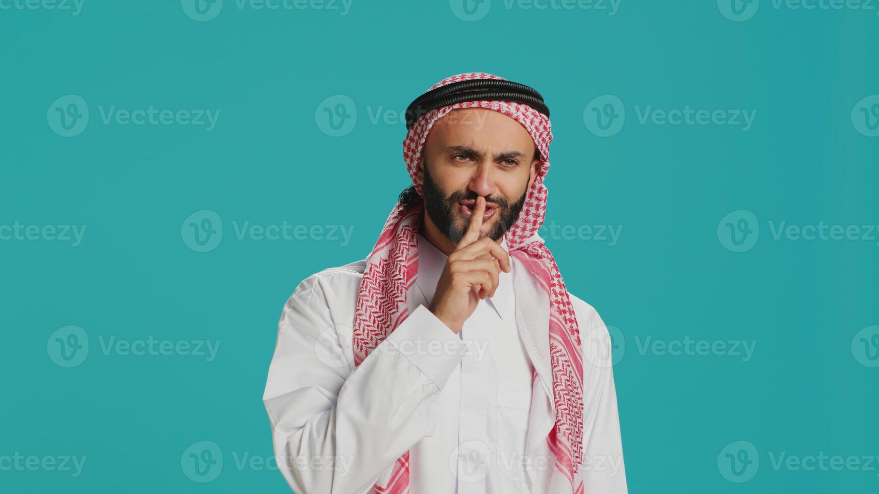 Arabic adult showing silence symbol with finger over lips, presenting hush mute sign on camera. Private person doing confidential secrecy gesture in studio, trying to keep secret. photo