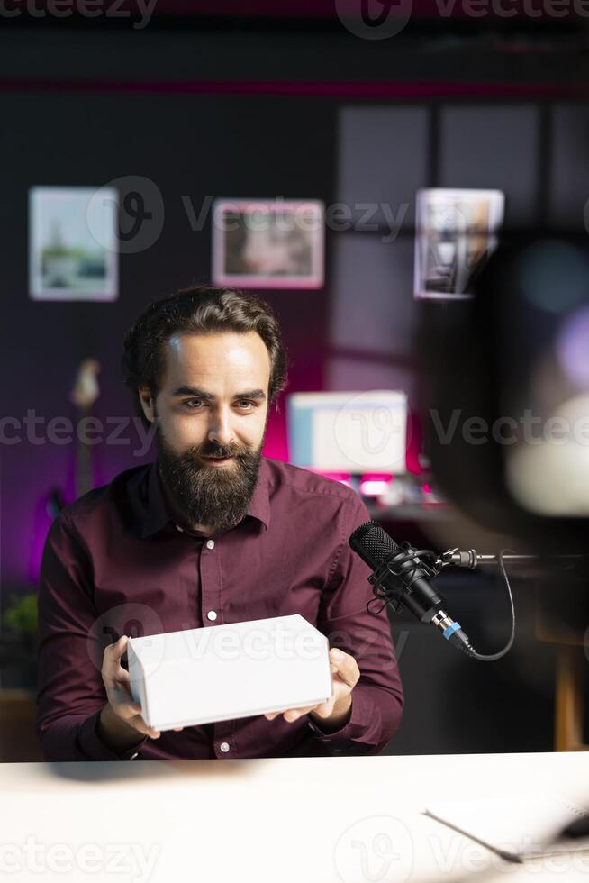 Man receiving mystery box from audience, ready to film packaged product unboxing. Online star presenting surprise package received, recording in studio with professional camera and mic photo