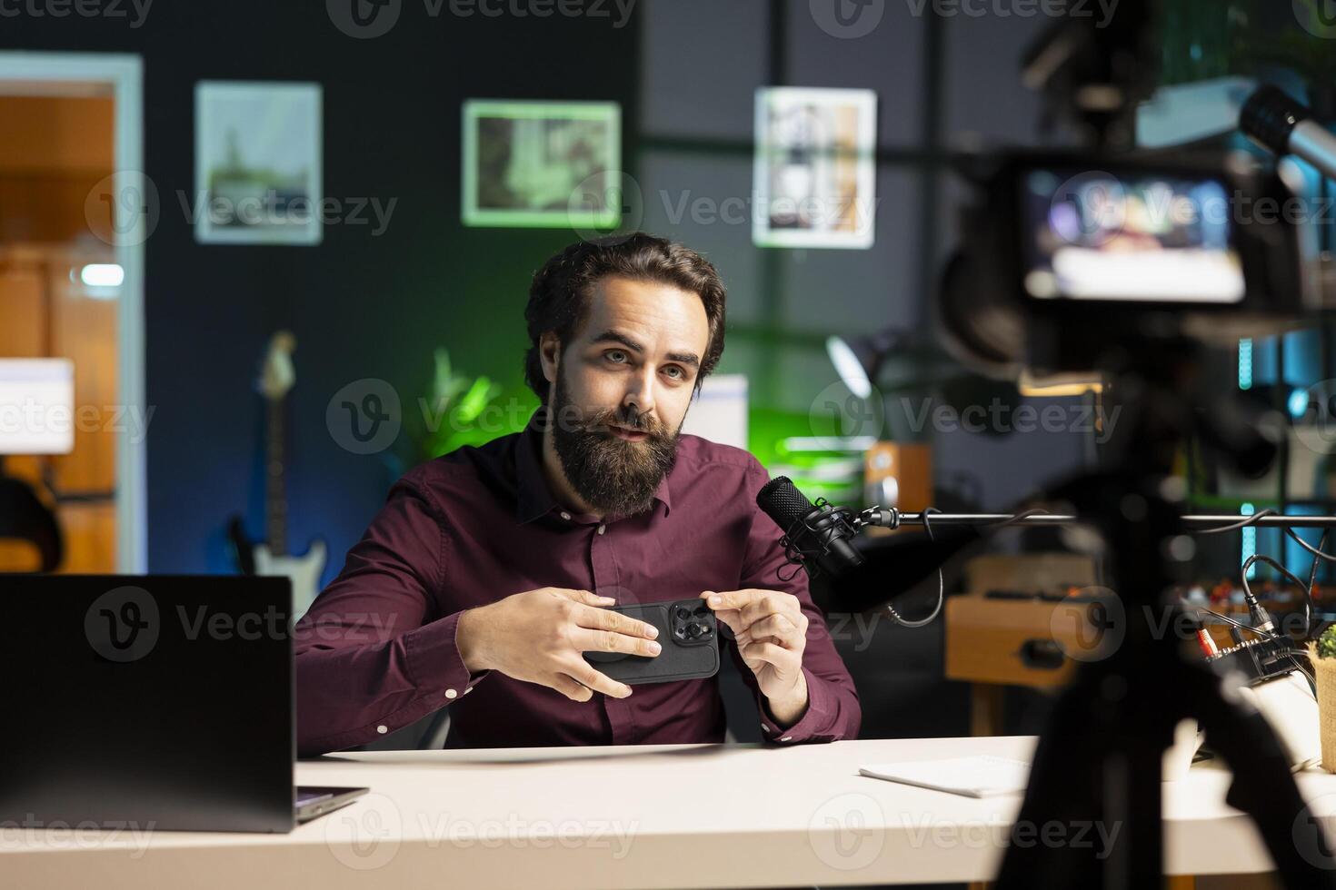 Entertainer presents mobile phone from brand sponsoring , urging viewers to purchase it, filming with professional camera. Man advertising smartphone to audience, recording with specialized gear photo