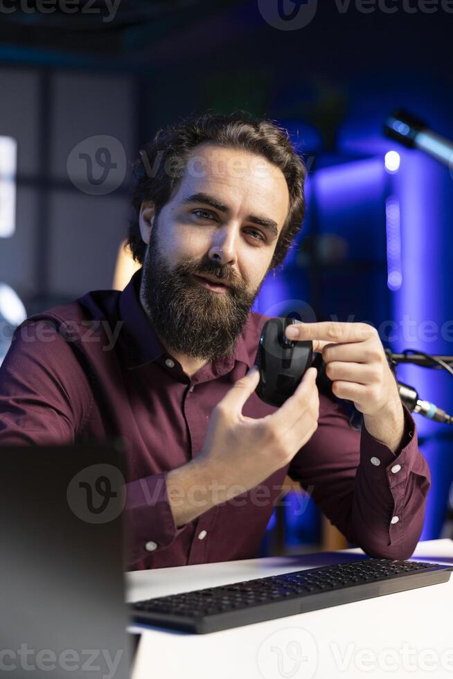 Smiling tech expert filming review for online channel in apartment studio, analyzing office mouse for audience. Happy content creator recommending computer peripheral device photo