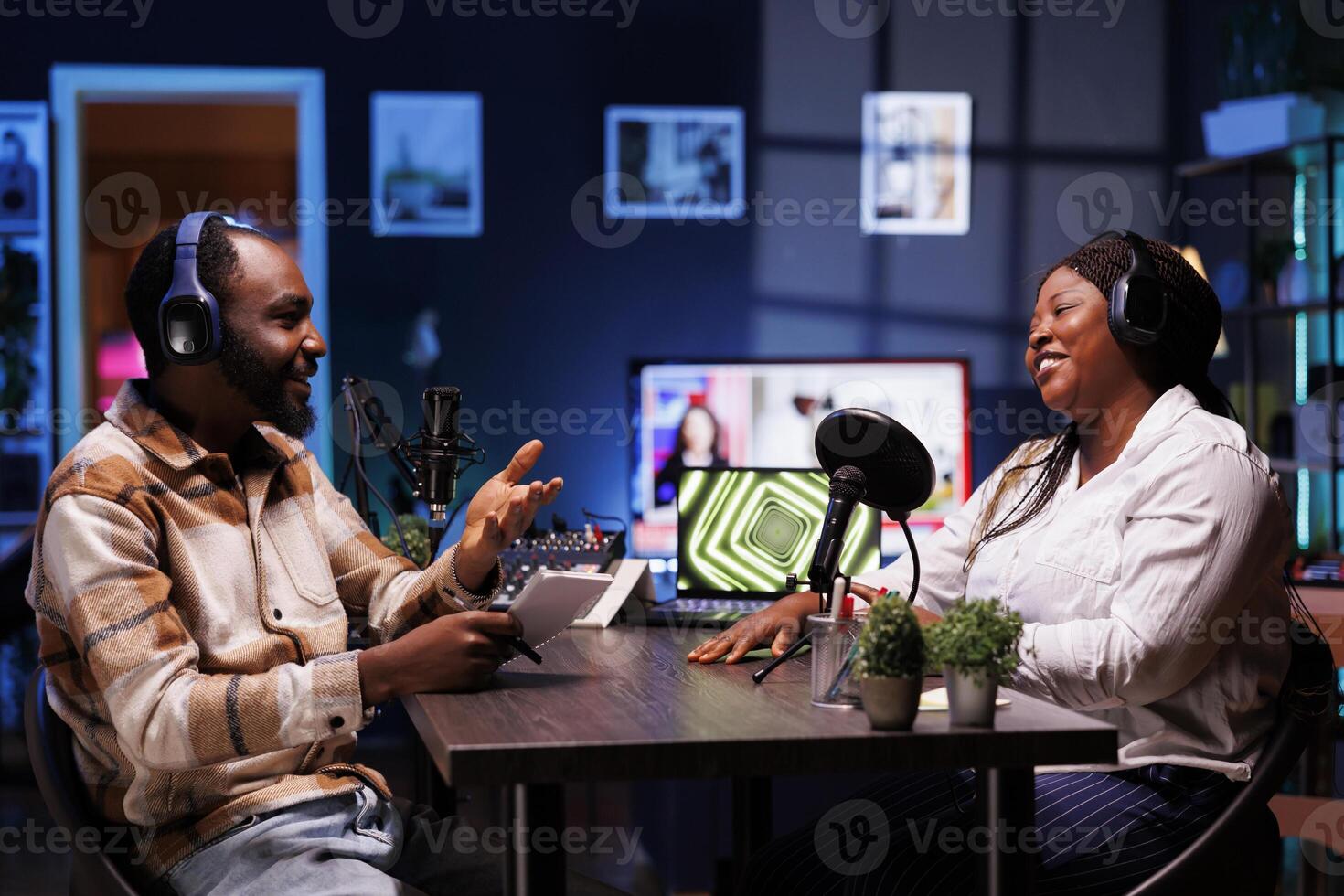 Podcasters enjoying happy conversations with online listeners in home studio, covering wide range of subjects. Man carrying notebook is speaking with socialite and they are having a good discussion. photo