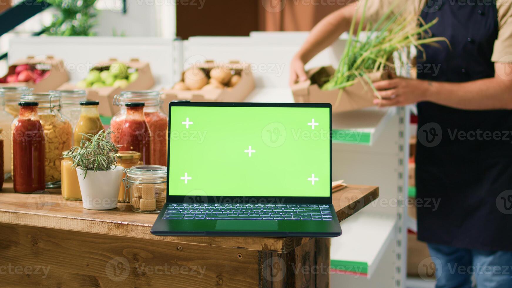 Laptop displaying greenscreen in bio shop filled with freshly harvested fruits and vegetables, sustainable lifestyle concept. Computer shows isolated chromakey template in zero waste store. photo