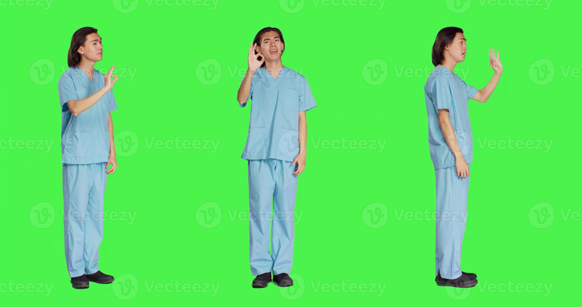 Medical assistant presents good sign over full body greenscreen backdrop, showing agreement and like gesture. Healthcare employee in uniform doing approval sign in studio. photo