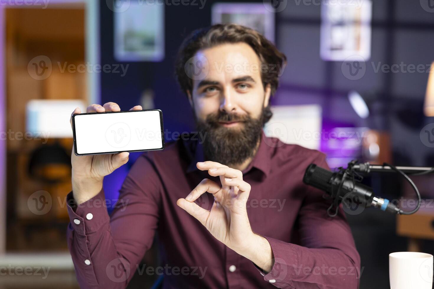 Man holding isolated screen smartphone in hand, using it as empty copy space to showcase his online streaming channel logo. Content creator does introductory using mockup mobile phone photo