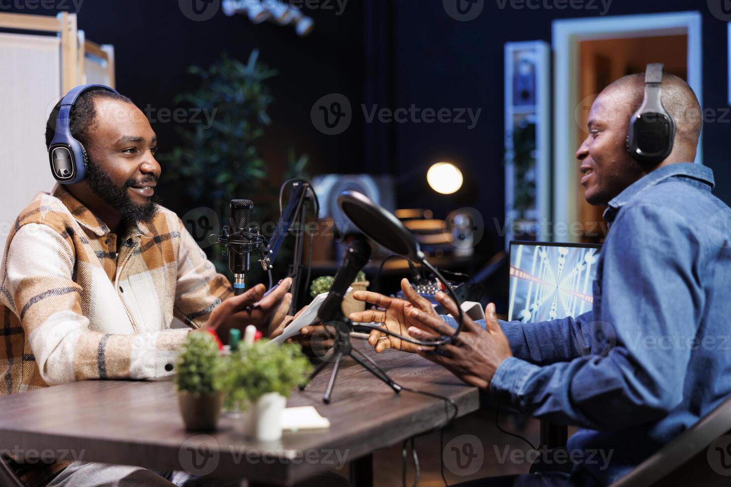 Serious talk between two black guys is being recorded for the online audience. Male African American content creators utilizing audio equipment while seated at home to make a podcast episode. photo