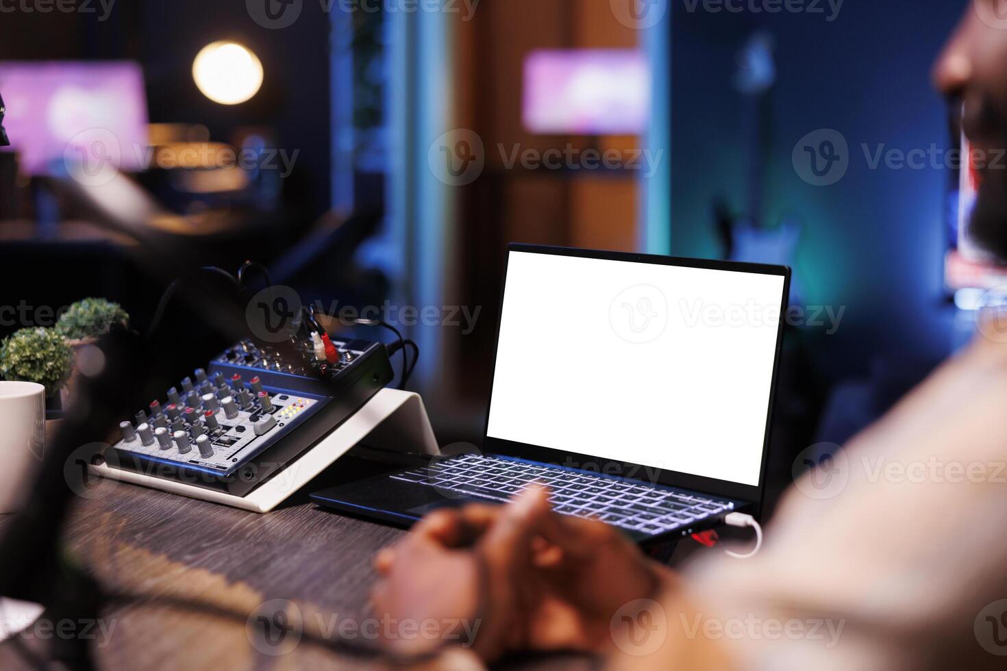 Electronic device near microphone audio mixer is displaying an isolated white screen. Digital laptop on table is showing a blank copyspace mockup template for podcast show advertisement. photo