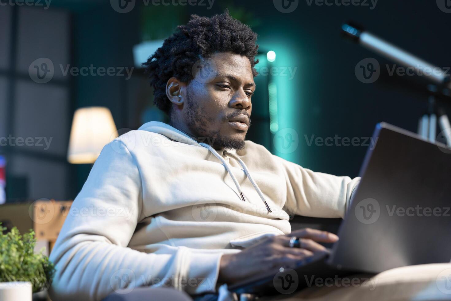 Self employed man working from home using laptop to send emails. African american man typing on notebook keyboard, composing documents in order to deliver finalized project to client photo
