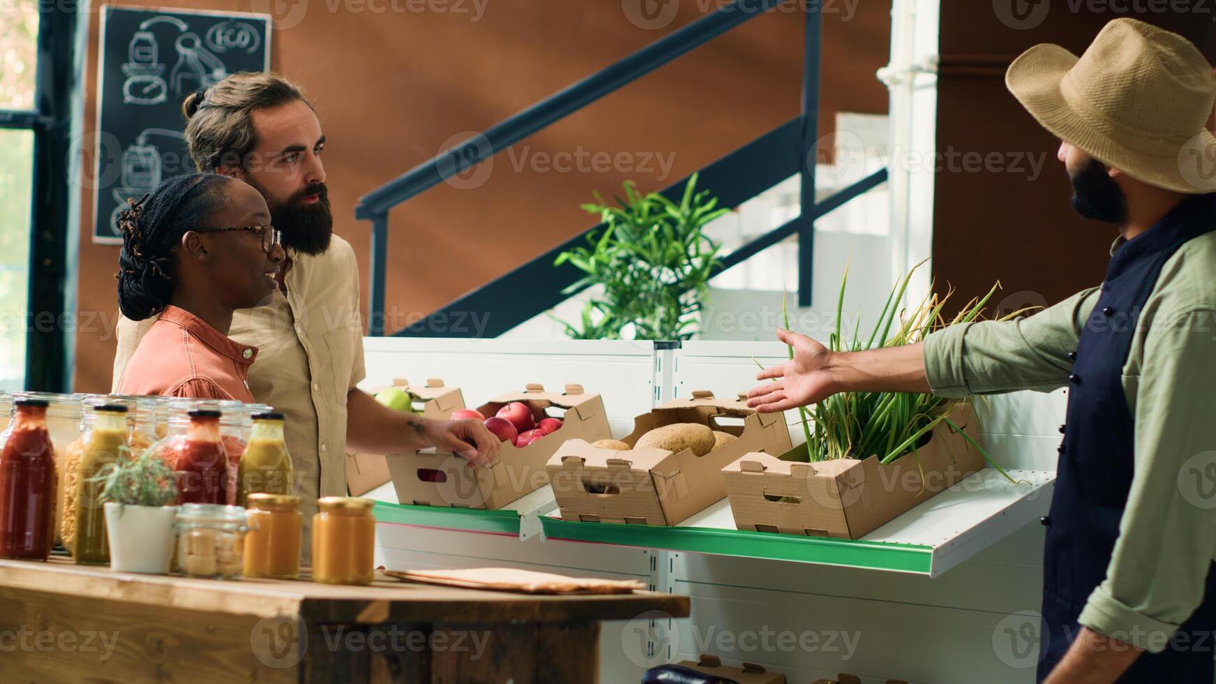 Vendor shows fresh produce to clients in local zero waste eco store, storekeeper recommending locally grown fruits and vegetables. Young farmer presenting chemicals free food. Handheld shot. photo