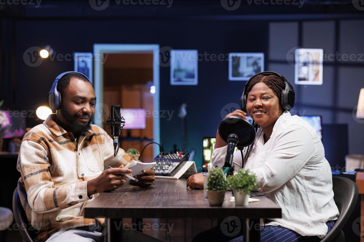 Black journalist uses modern recording technology to interview smiling female content creator in home studio. They broadcast their lively conversation to online audience via social media platforms. photo