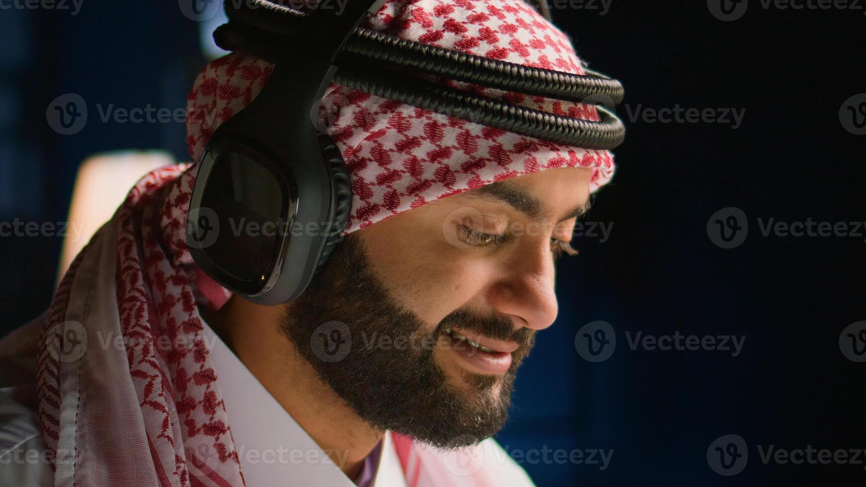 Extreme close up shot of arabic employee with wireless headphones in office sending emails. Muslim worker surfing the net doing research using laptop while listening to music to make time pass faster photo