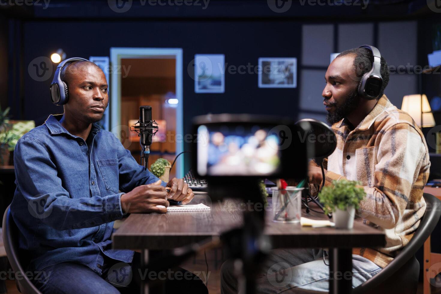 Content creators sitting at table, recording material with professional camera at home. Online show host conducts friendly chat with media star while filming with device mounted on tripod. photo