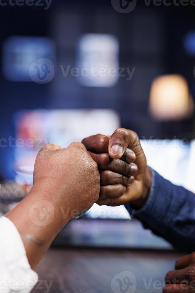 Detailed view of african american individuals fist bumping with each other in apartment. Surrounded by neon lights are black people at the table, using hand gestures for greetings. photo