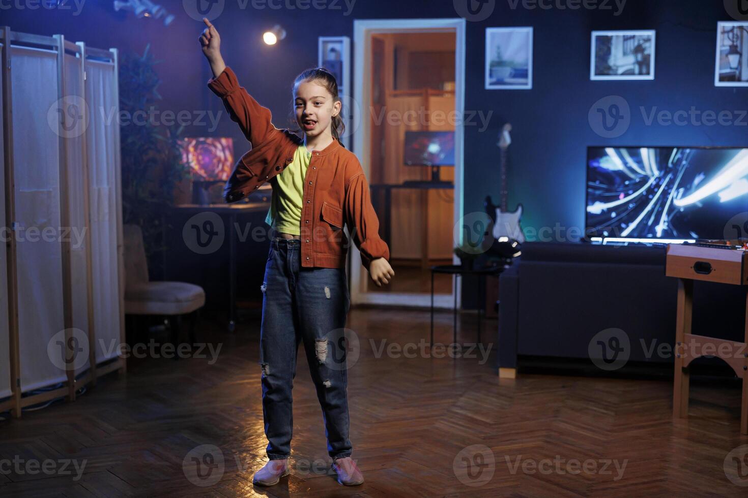 Child in dimly lit apartment doing viral dance for social media platforms viewers while listening to popular hit song. Energetic generation Z girl recording dancing on latest viral music photo