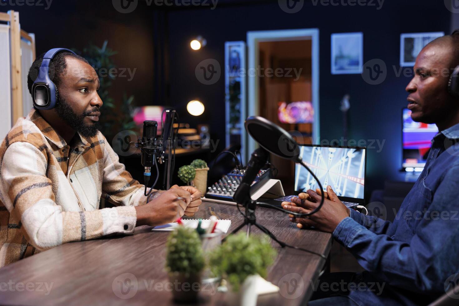 Black man hosting radio program is having live conversation with male guest, recording the encounter for audience to listen. Influencer making a podcast with journalist using audio equipment. photo
