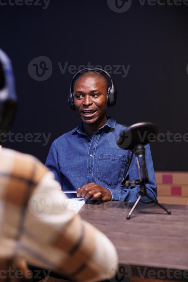 Black male guest speaking into microphone, answering questions from radio program host. African american man being interviewed using audio equipment to record an online talk show at home. photo