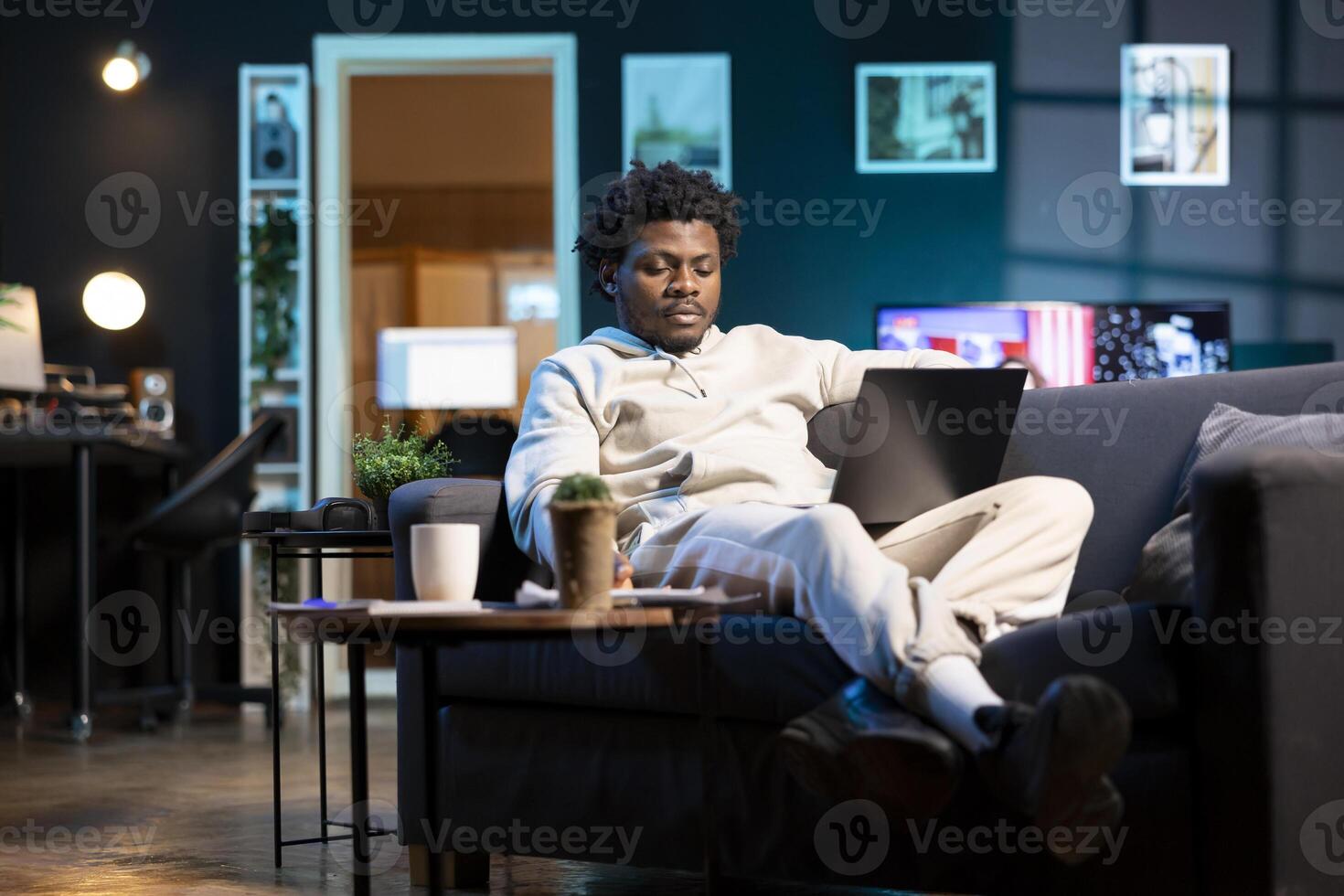 African american man at home paying attention in elearning seminar teleconference with teacher, writing on notepad. Homeschooling student listening to lesson on laptop while doing his homework tasks photo