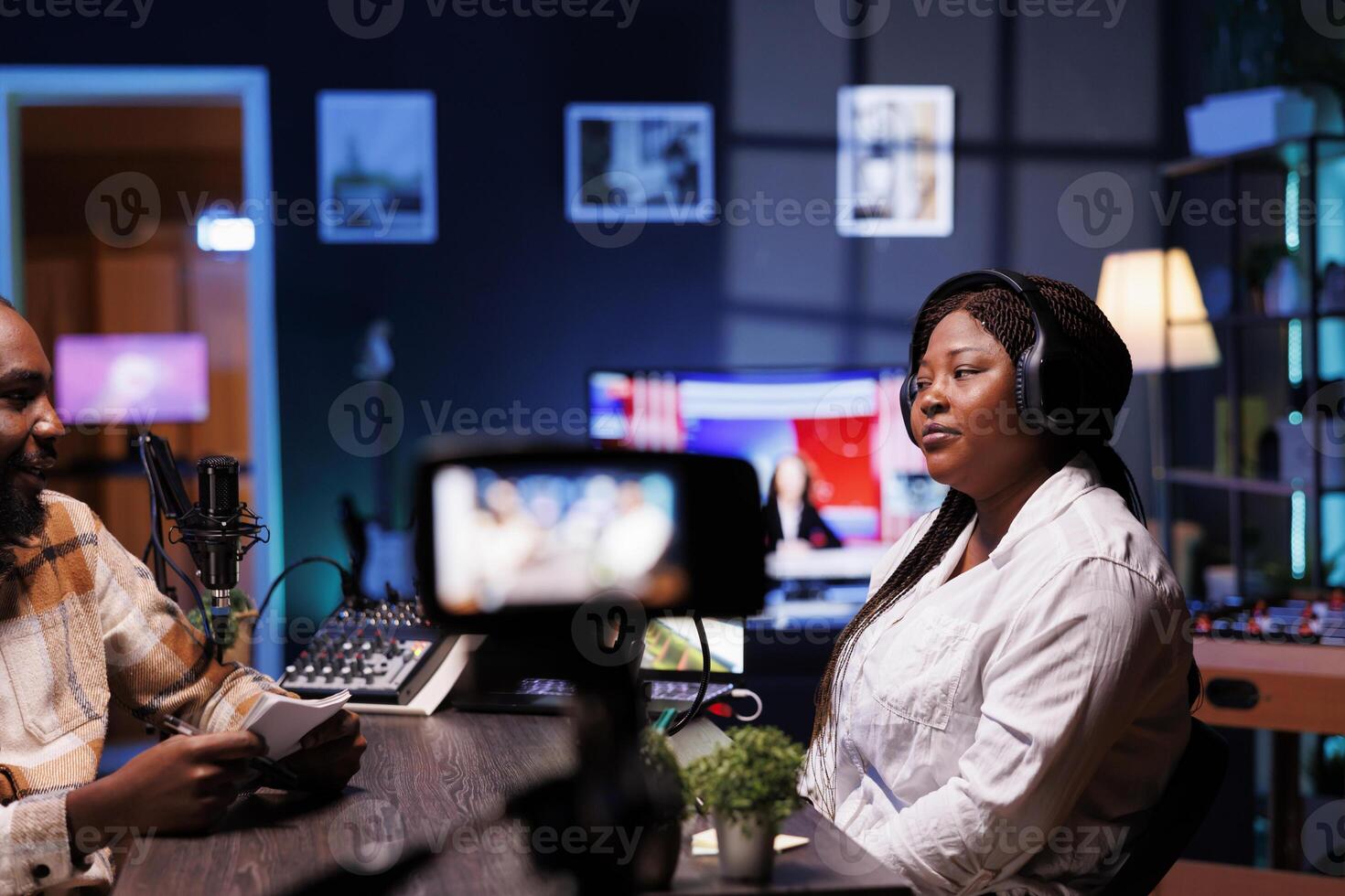 During a vlog recording session, a man is using a professional microphone and audio mixer while interviewing an African American female influencer in front of a digital camera. photo