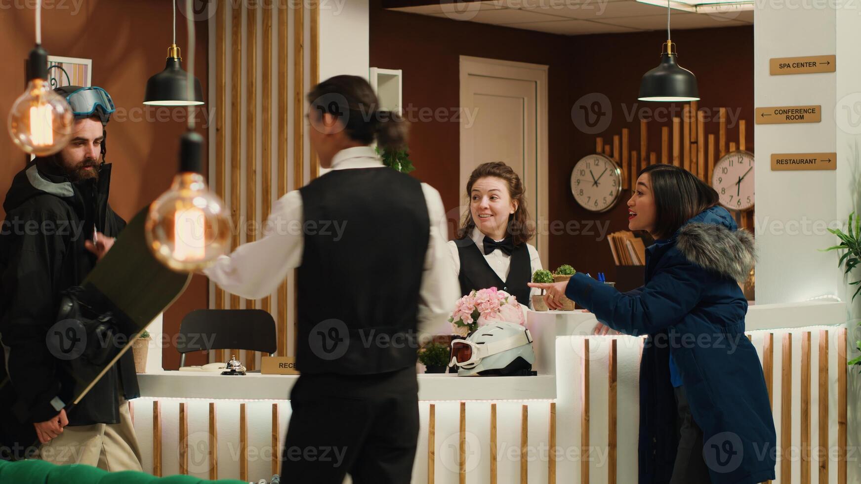 Active couple in winter outerwear stands in hotel reception during holiday, receptionists greeting tourists. Visitors with skiing and snowboarding gear ready for alpine adventures at ski resort. photo