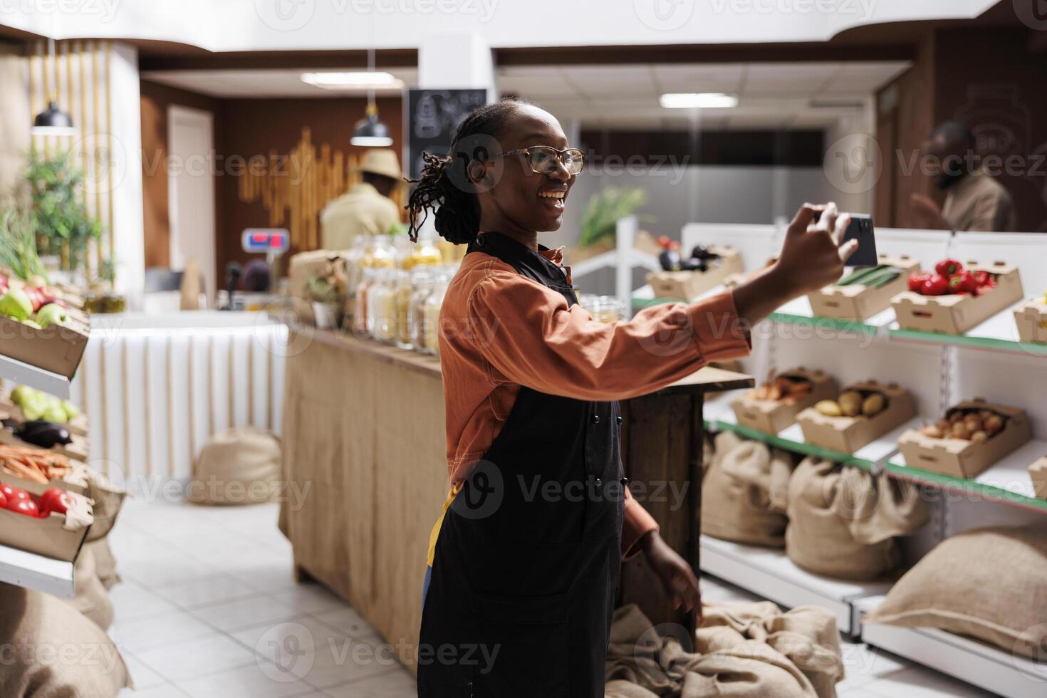 side view shot of a vendor filming a to showcase variety of nutritious, fresh food options. Using her smartphone, she engages with customers through social media and promotes healthy lifestyle. photo