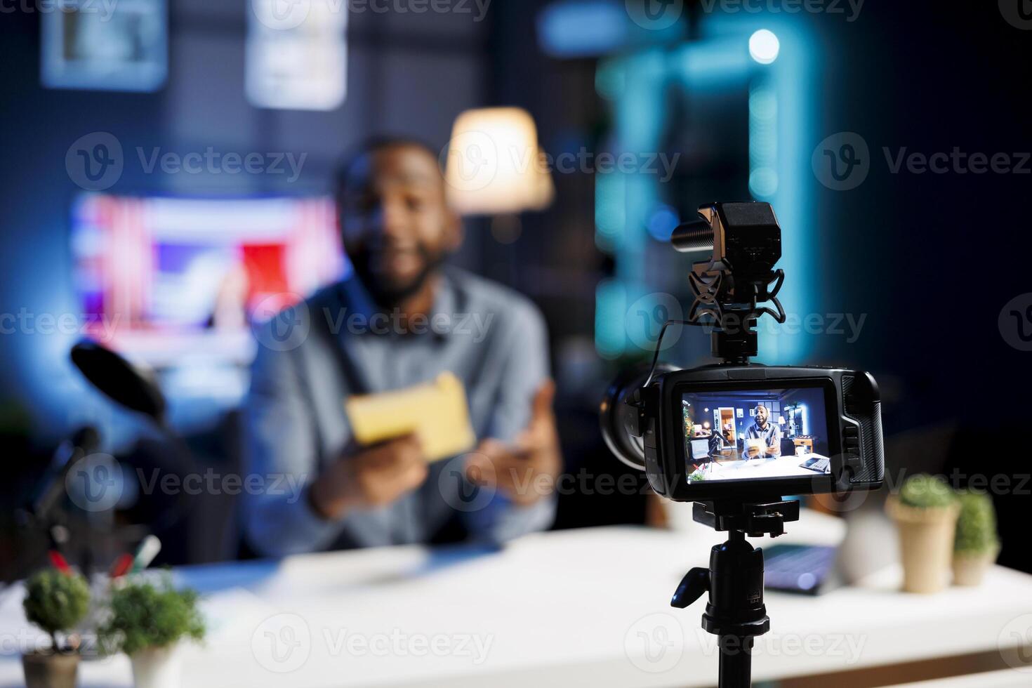 Focus on professional production camera used for capturing footage of man in blurry background filming literature critique for online readers audience, showcasing new book from publisher photo