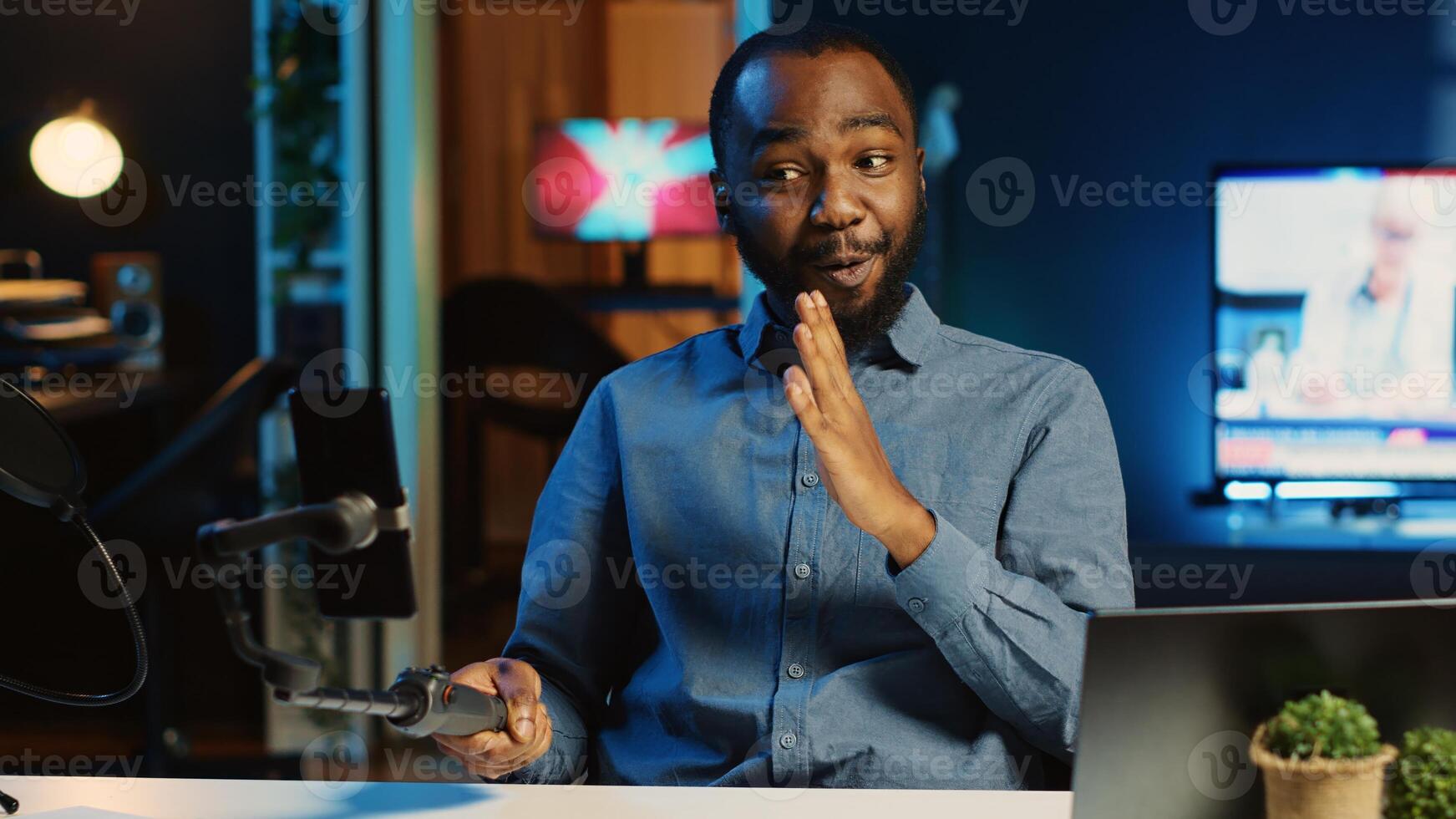 African american content creator using selfie stick smartphone, doing live broadcast for subscribers showing his new home studio design. Online star films himself for viewership using cellphone camera photo